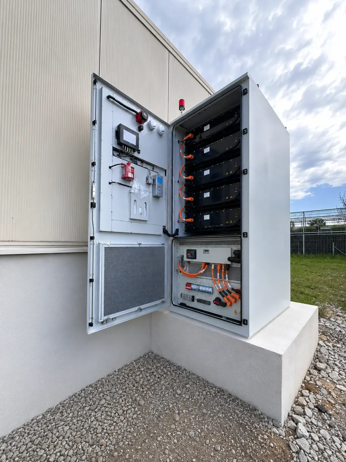 ENERGRID M261 με ανοιχτές πόρτες: στα δεξιά τα battery packs σε ράφια με πορτοκαλί καλώδια ισχύος, στα αριστερά ο πίνακας ελέγχου και ο εξοπλισμός πυροπροστασίας.